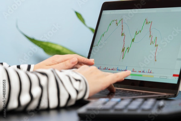 Fototapeta A falling graph on a laptop monitor and hands ready to make a share purchase deal.