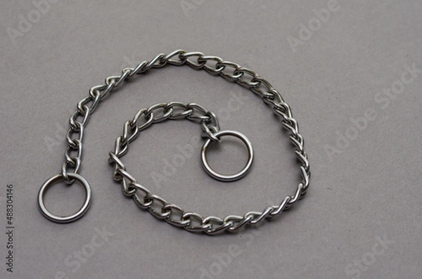 Obraz Silver metal chain with two rings on a gray background. Tugging dog leash.