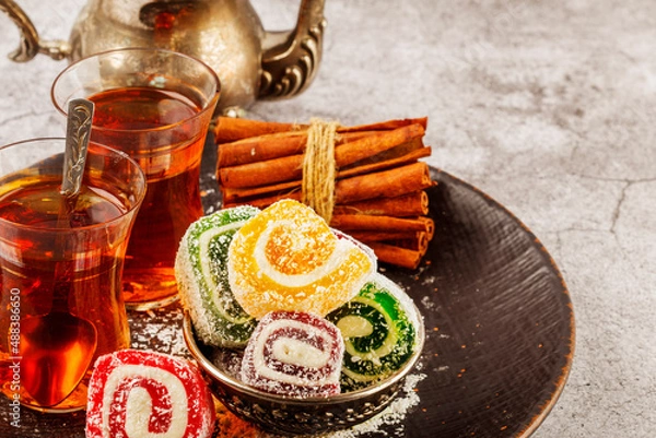 Fototapeta Traditional Turkish delight with Turkish tea on gray background. Ramadan Kareem celebration concept. Fragrant Turkish tea and Turkish sweets in national dishes.