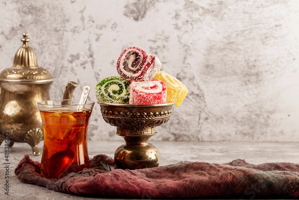 Fototapeta Traditional Turkish delight with Turkish tea on gray background. Ramadan Kareem celebration concept. Fragrant Turkish tea and Turkish sweets in national dishes.
