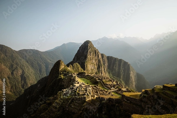 Obraz World-famous Inca city of Machu Picchu during sunrise with yellow light rays and misty clouds (without any visitors) (Aguas Calientes, Peru, South America)
