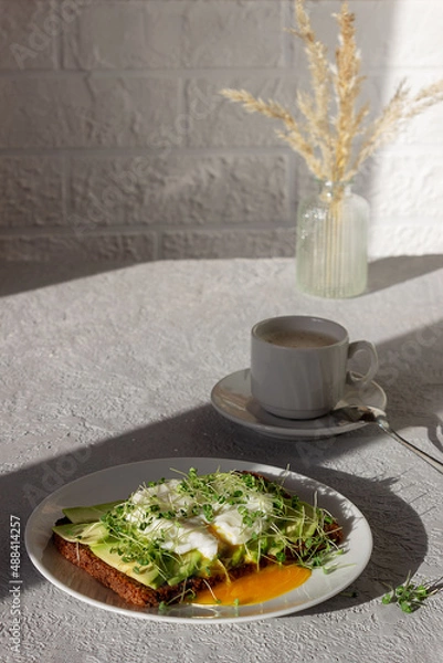Fototapeta Healthy breakfast, toasted whole grain bread with avocado, poached egg, microgreens and a cup of coffee