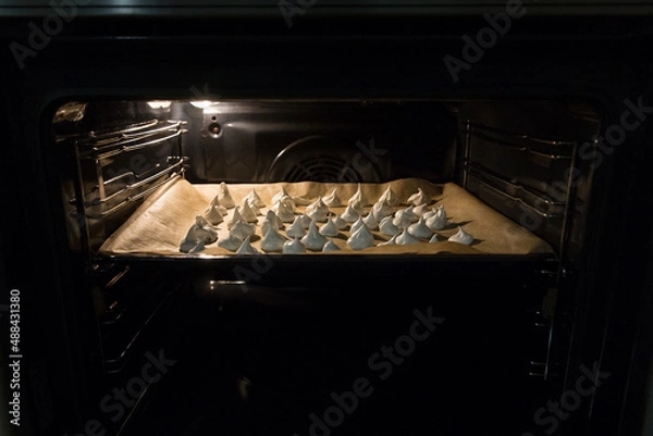 Obraz Meringue is baked on a baking sheet covered with parchment paper in the oven