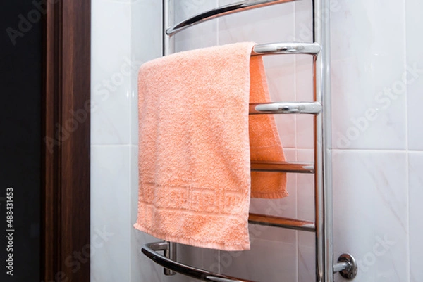 Obraz orange terry towel hanging on a chrome heated towel rail in the bathroom