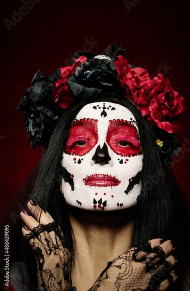 Fototapeta portrait of a beautiful woman with a sugar skull makeup with a wreath of flowers on her head, red background