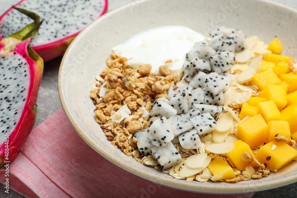 Fototapeta Bowl of granola with pitahaya, mango and yogurt on table, closeup