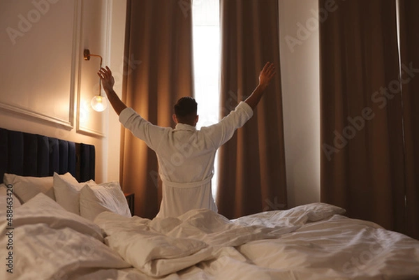 Fototapeta Man waking up in hotel room, back view