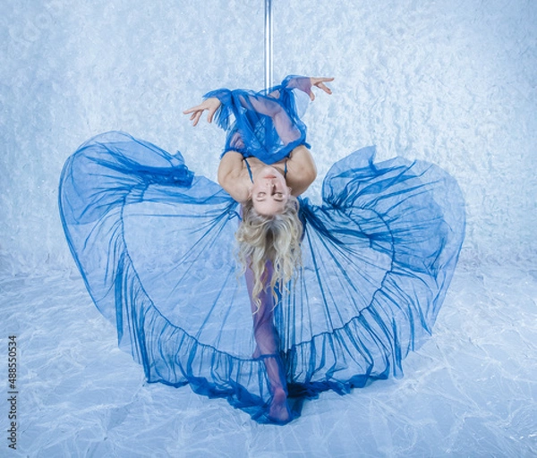 Fototapeta Poledens blonde with a beautiful figure, long legs, a dancer in a blue beautiful outfit sits beautifully and gracefully on a pylon
