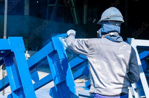 Fototapeta The painter uses a spray gun to paint a steel structure before transportation to the assembly yard.