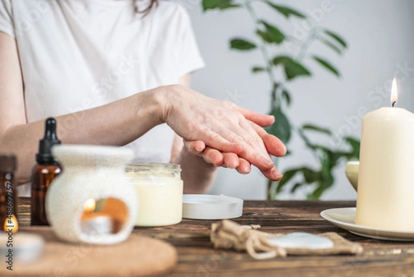 Obraz Woman is smearing her hands with a natural organic cream doing a massage. Aroma lamp with essential oils and candles on the table. Concept of skin and self care in atmosphere of harmony and relaxation