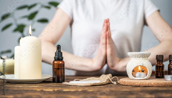 Fototapeta Aroma lamp with essential oils, burning candles and a woman with her hands folded in a namaste pose. Concept of evening and morning rituals, meditation, harmony and balance