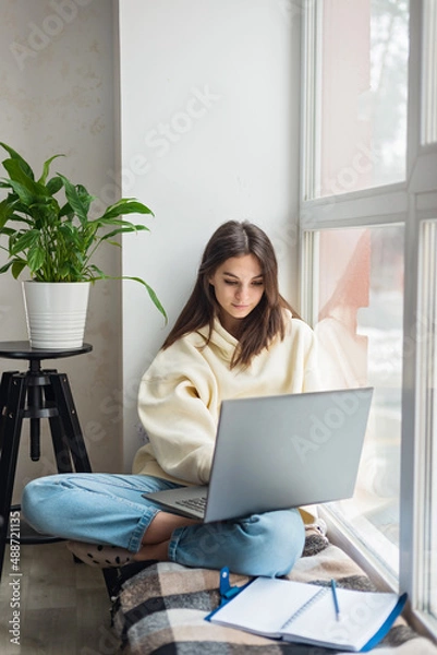 Fototapeta Teenager school-girl pupil distance learning online at remote virtual class, preparing for exams, watching webinar, zoom meeting lesson on laptope at home. Soft selective focus.