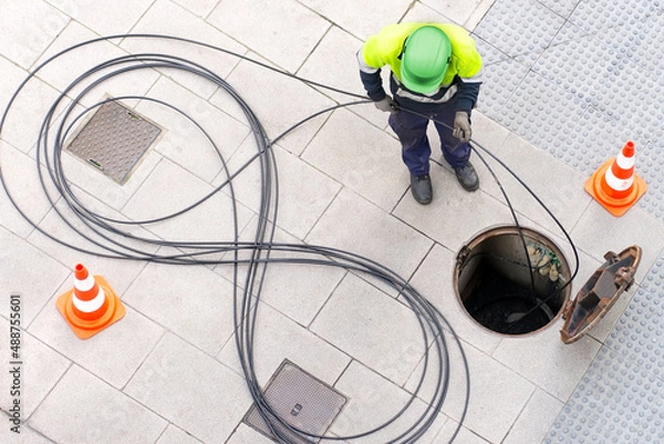 Obraz electrician worker install optical fiber cable for internet and telephone underground lines  in city street