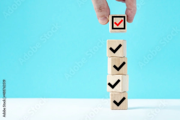 Fototapeta Hand takes a cube with a wooden block. Check mark on wooden blocks, blue background