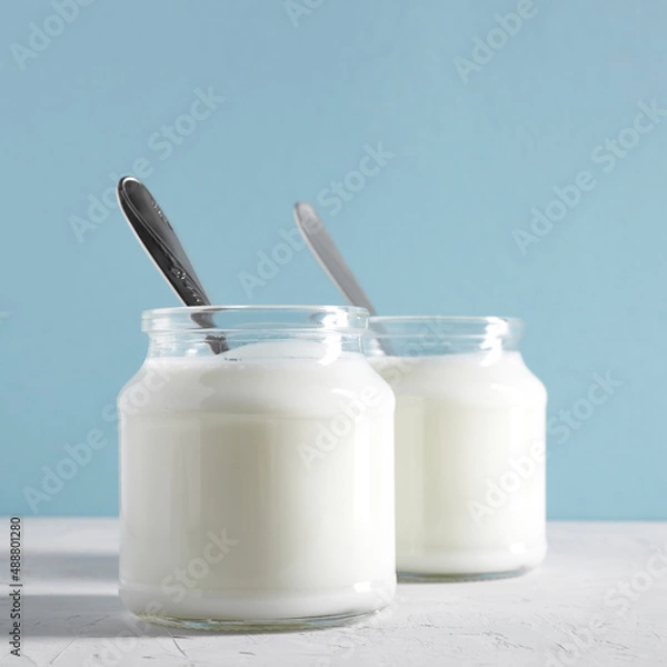 Obraz Yogurt, kefir or fermented milk product in glass jars on a white table. White and blue background. Healthy food concept