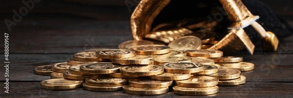 Obraz A bag with gold coins on a wooden background. The money is in a black bag. Treasure Hunt. A Purse with money. Wallet wit gold coins.
