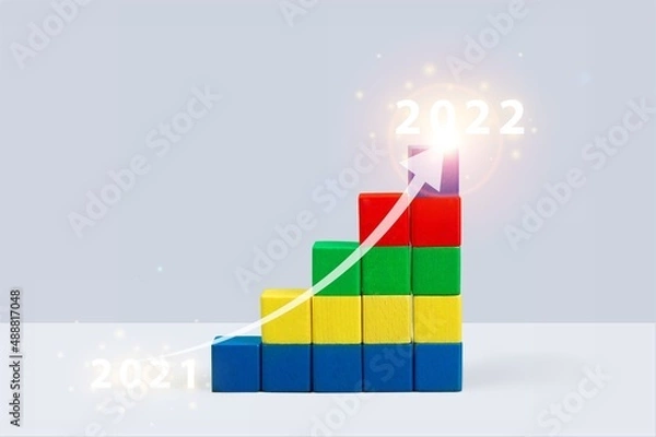 Fototapeta Shining rise up arrow on wooden blocks chart steps from the year 2021 to 2022. The business growth process