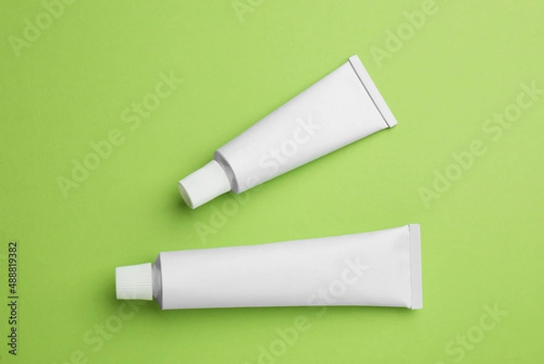 Fototapeta Blank white tubes of ointment on light green background, flat lay. Space for text