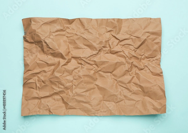 Fototapeta Sheet of crumpled brown paper on light blue background, top view