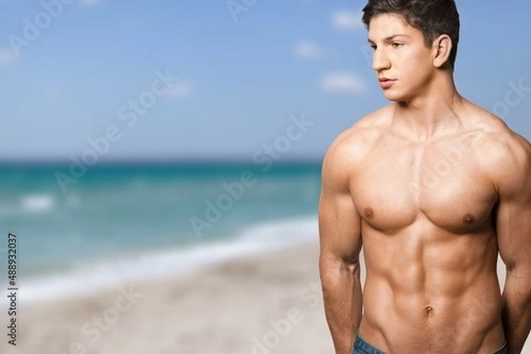 Fototapeta Sexy portrait of muscular handsome topless male model at the beach background.