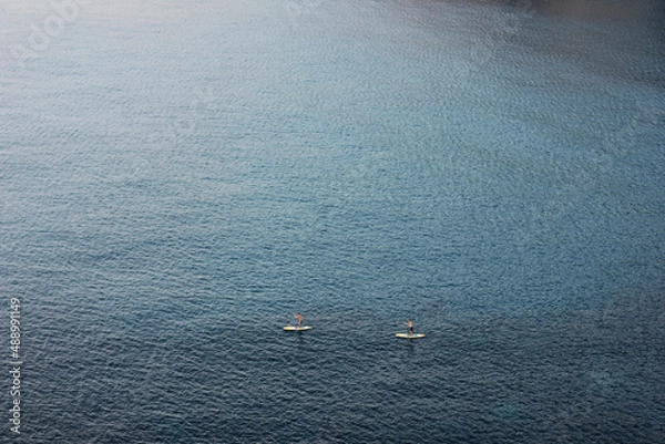 Fototapeta Two unrecognizable people stand up paddling on the ocean from high angle view with yellow boards