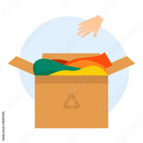 Fototapeta Cardboard box with old clothes for recycling and donating. The hand throws the clothes into the box