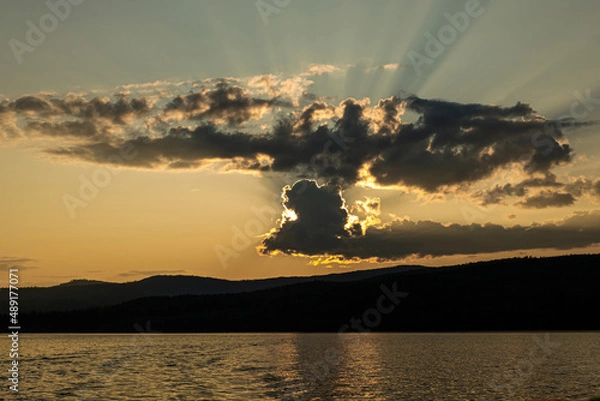 Obraz sunset on the background of mountains the rays of the sun break through the beautiful clouds