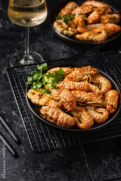 Fototapeta Grilled shrimp with garlic and parsley. Spiked shrimp-bear on a plate with a glass of white wine. Bering shrimp. Menu concept for restaurants. Dark photo.