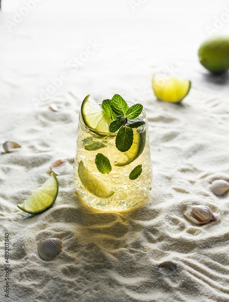 Fototapeta Summer healthy lemonade, cocktails of citrus infused water or mojitos, with lime, ice and mint, diet detox beverages, in glasses on a summer beach.
