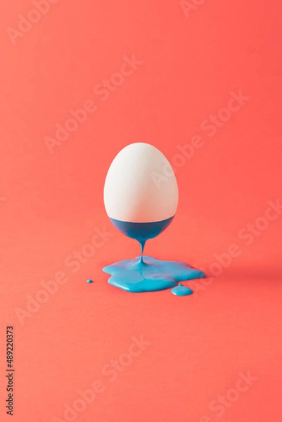 Fototapeta Surreal composition with levitating white egg and blue liquid on pastel red background.