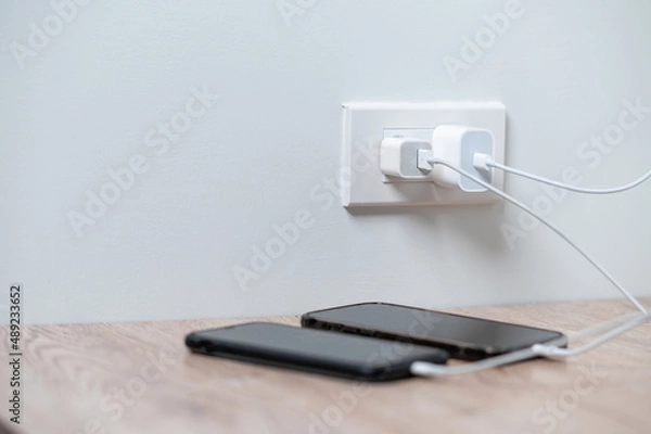 Fototapeta smart phone charger plugged on wooden with plugged at home.