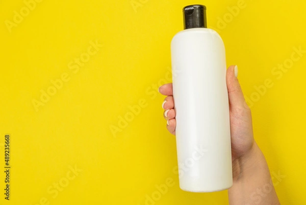 Fototapeta Cleaner's hand holding a  chemical spray bottle. Empty space for text or logo on a yellow background. Early spring or regular cleaning. Cleaning and cleaning concept. flat lay