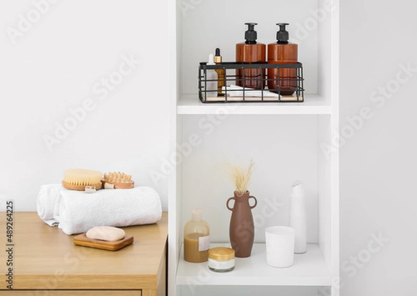 Fototapeta Shelf unit and table with different bath supplies near white wall