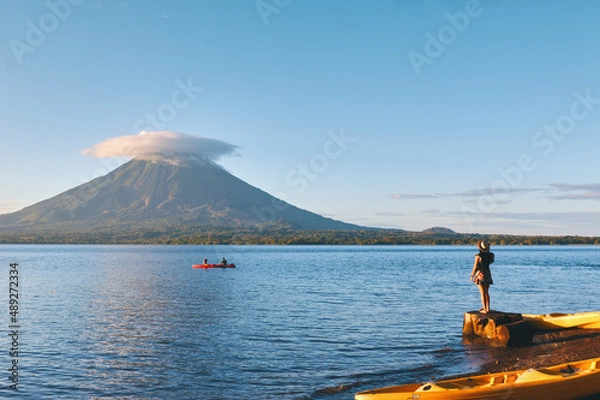 Obraz Young woman wearing hat standing on the shore of the lake with beautiful view to Concepción volcano in Ometepe island, Nicaragua.