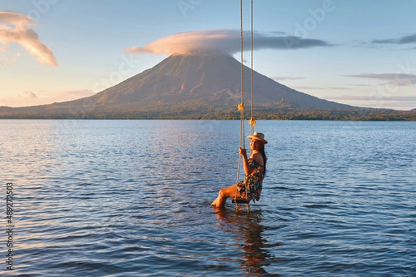 Obraz Woman sitting on swing in the lake with a beautiful view to the concepcion volcano during sunset in Ometepe island, Nicaragua