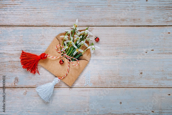 Fototapeta Bouquet of delicate snowdrops in an envelope on a wooden background with Martisor talisman and number one. First of march celebration Baba Marta Day. Space for text.