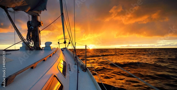 Obraz White yacht sailing in an open sea at sunset. A view from the deck to the bow, mast, sails. Epic cloudscape. Dramatic sky with glowing golden clouds after the storm. Racing, sport, leisure activity