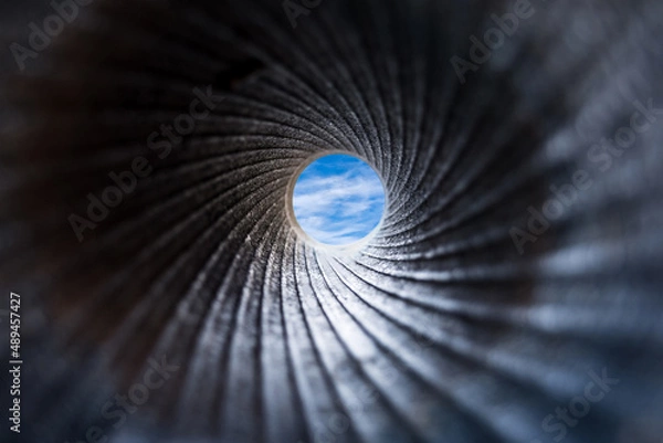 Fototapeta A view through a dark barrel of cannon to the blue sky with white fluffy clouds. Close up, selective focus. Abstract background concept