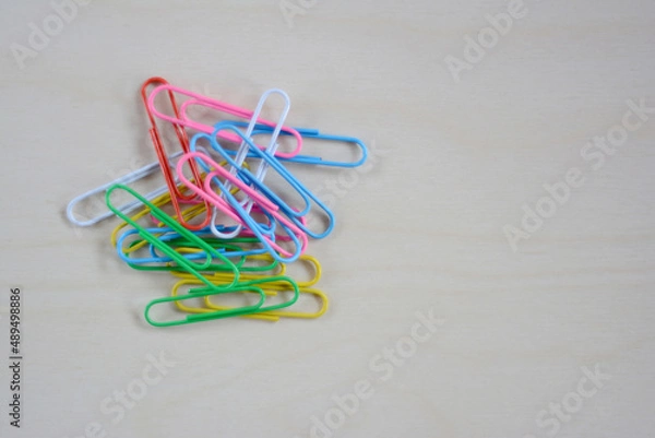 Fototapeta multi-colored paper clips are scattered on a wooden board: