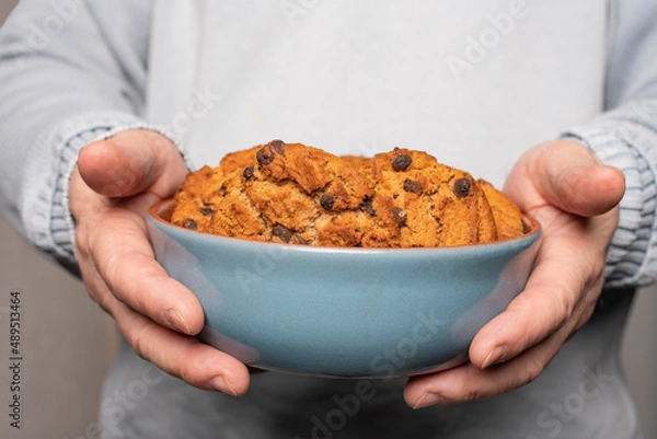 Fototapeta A young man holds a plate with homemade cookies with raisins, chocolate, nuts. Breakfast. Close.