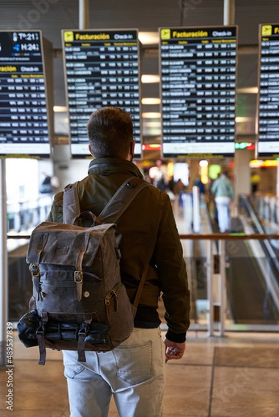 Obraz young digital nomad with a backpack looks at the flight schedule