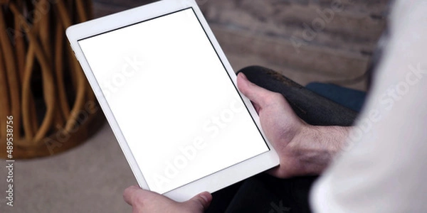 Fototapeta A tablet with empty white screen, close up on man hands while using an apple iPad with blank touch screen.