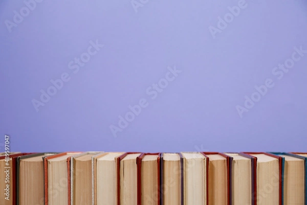 Fototapeta Composition with vintage old hardback books, diary, fanned pages on wooden deck table and colored background. Books stacking. Back to school. Copy Space. Education background.