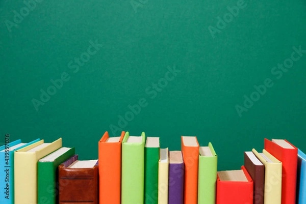 Fototapeta Composition with vintage old hardback books, diary, fanned pages on wooden deck table and colored background. Books stacking. Back to school. Copy Space. Education background.