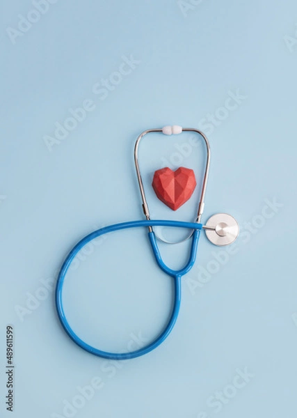 Fototapeta Stethoscope and red polygonal heart on blue background. Vertical banner for medical clinic or center, copy space