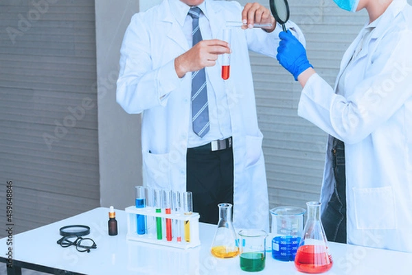 Fototapeta Scientist team in uniform holding beaker and test tube have chemical liquid for testing chemical reaction.