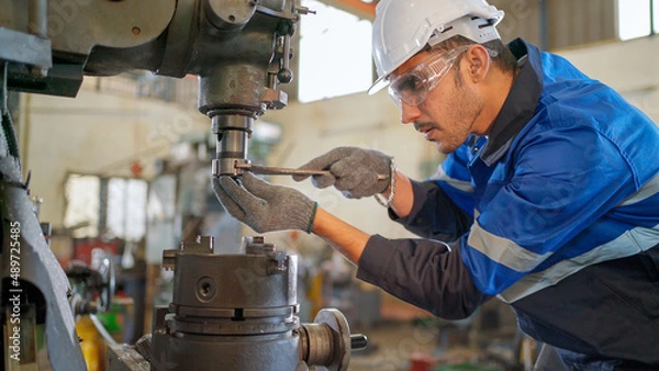 Obraz Engineer man checking the status of machine and used wrench to screw some part of equipment at CNC factory. Worker wearing safety glasses and helmet. Maintenance and repairing concept.
