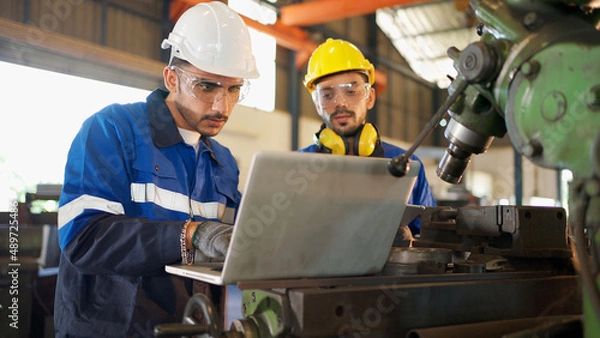 Fototapeta Two engineers man standing in front of equipment in CNC metal machine factory. Manager looking at tablet and see information how to fix the equipment and explain detail. Discuss and repair