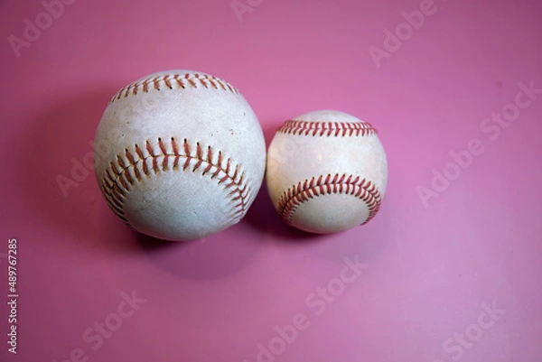 Fototapeta Softball next to a Baseball with a pink background.