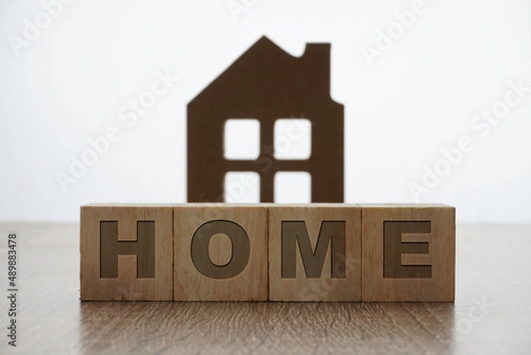 Fototapeta home wording on a wooden block with a house replica as background